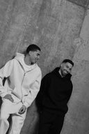 Two individuals wearing hoodies against a textured wall.
